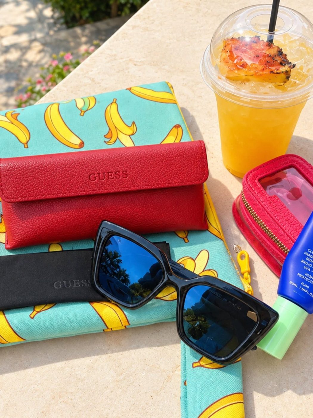 Guess sunglasses with a summer drink and beach accessories